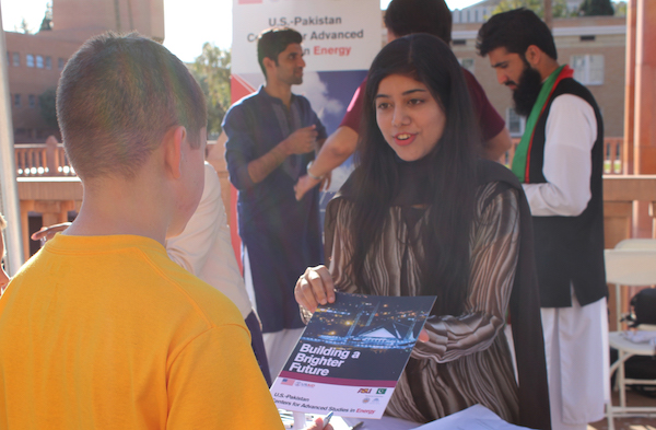 Photo of student showing a brochure to a child with a caption of "Farah Akram explains to members of the public what USAID’s mission is in Pakistan at Tempe Night of the Open Door. Photographer Erika Gronek/ASU"