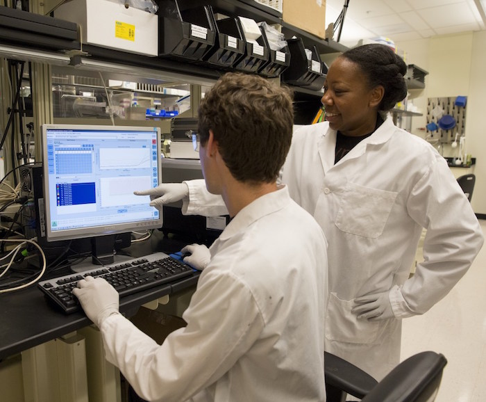 Photo of two people in lab coats looking at a computer monitor