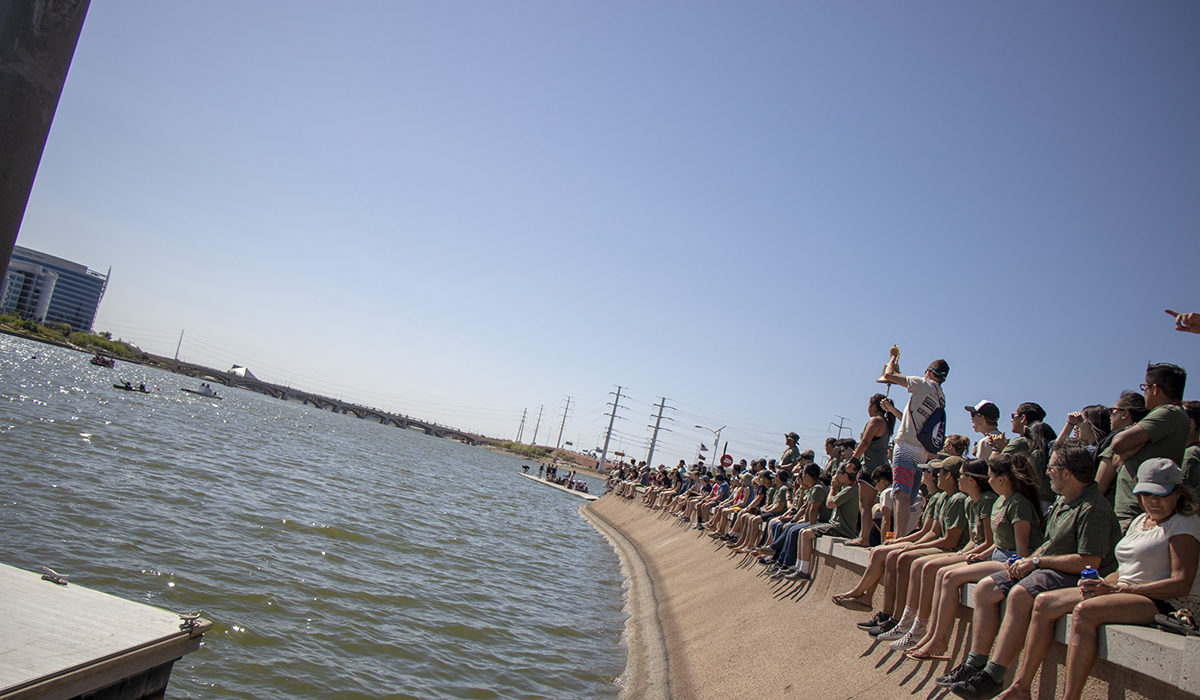 Photo of people sitting on the shore. Caption: Students from 18 universities, along with some of their family members, friends and alumni of their schools, gathered along the banks of Tempe Town Lake to cheer on students in the concrete canoe competition. Photographer: Marco-Alexis Chaira/ASU