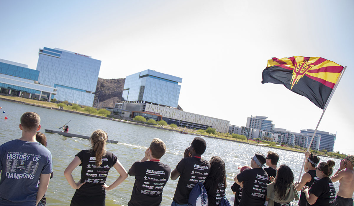 Photo of a group of people looking out onto the water. Caption: ASU students shouted encouragement and waved a university flag in support of the Ira A. Fulton Schools of Engineering students participating in the concrete canoe contests. Photographer: Marco-Alexis Chaira/ASU