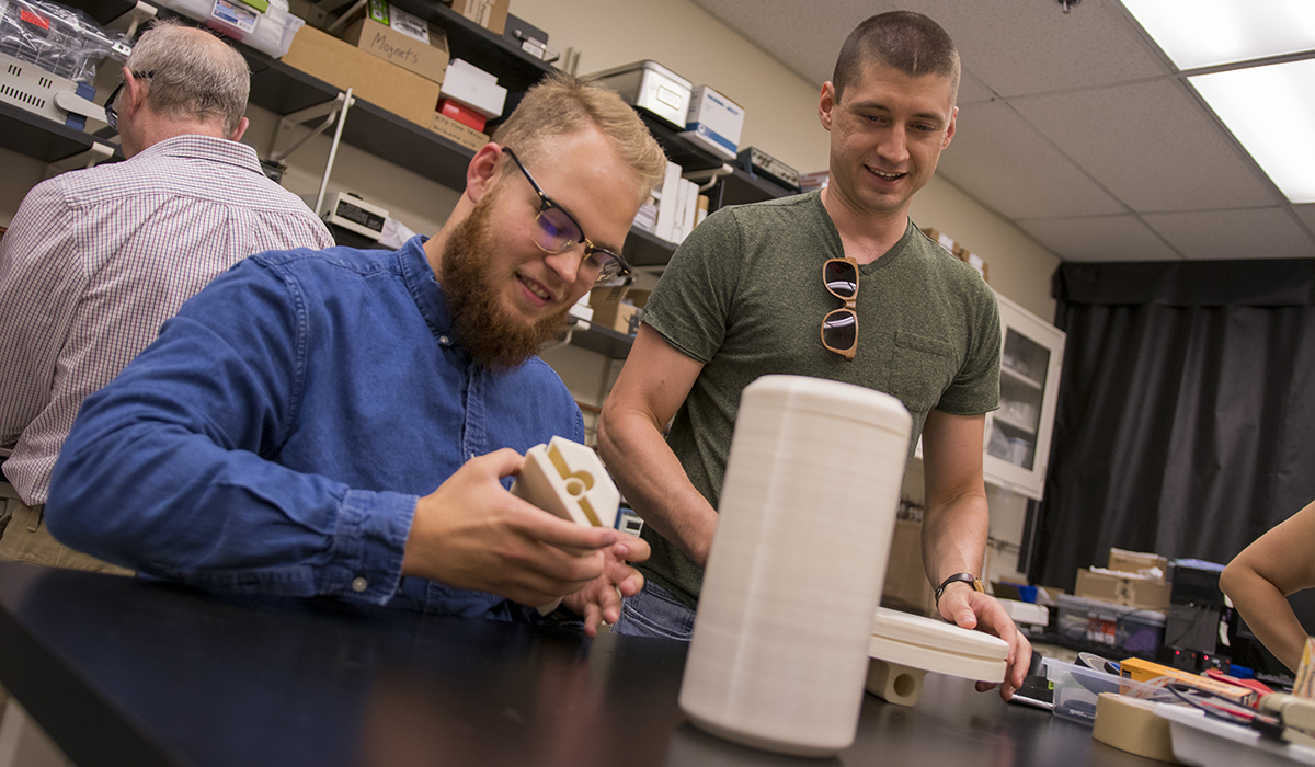 SenSIP-REU-Lab-2018-MAC0030w one student sitting and looking at object, one student standing
