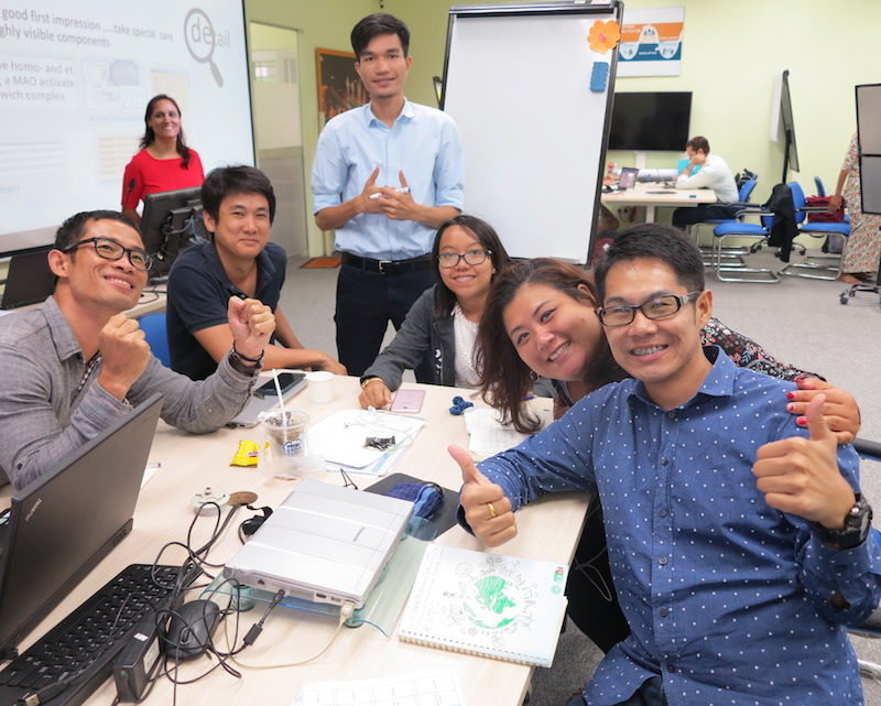 man standing at table with five others sitting