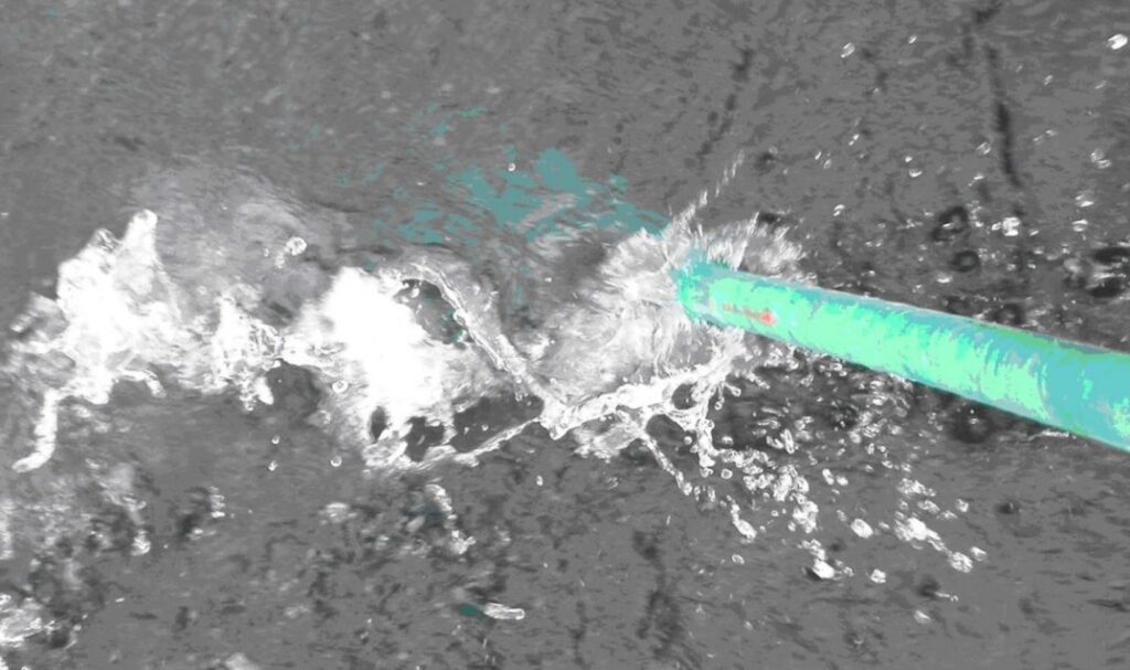 top-down view of a green pipe being moved in a wave pattern in flowing gray water.